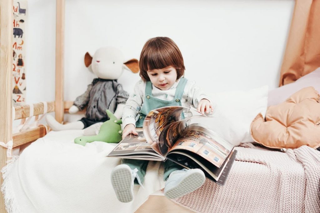 Leitura criança sentada na cama lendo.