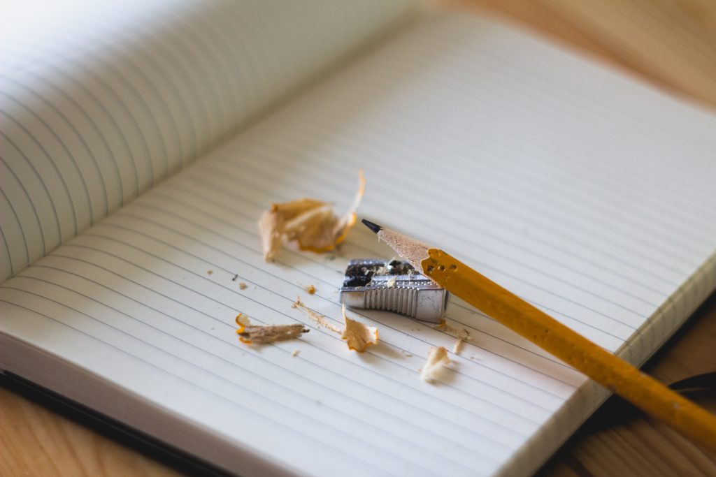 Foco na ponta de um lápis apoiado em um apontador, ambos sobre um caderno.