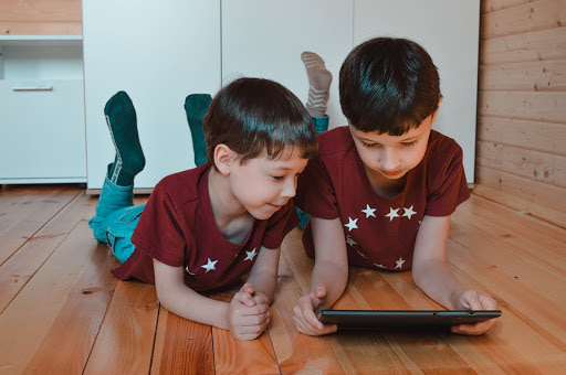5 cuidados para a educação a distância em tempos de pandemia duas crianças deitadas no chão brincando com um tablet.