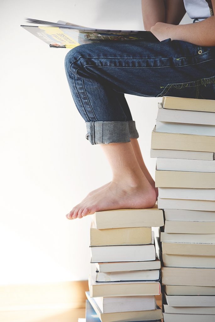 Criança praticando interpretação de texto em inglês, sentada em uma pilha de livros.