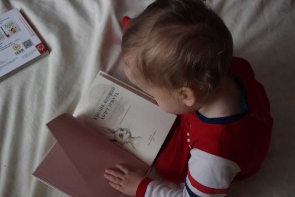 Bebê lendo um livro infantil, representando as fases da criança.