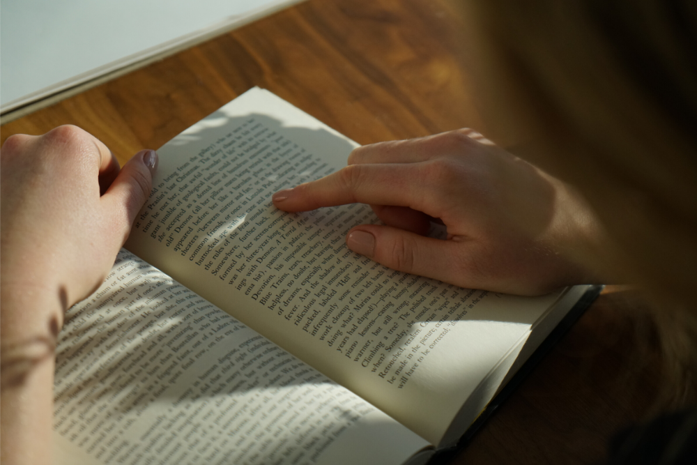 Pessoa fazendo interpretação de texto em inglês, lendo um livro iluminado pela luz do sol.