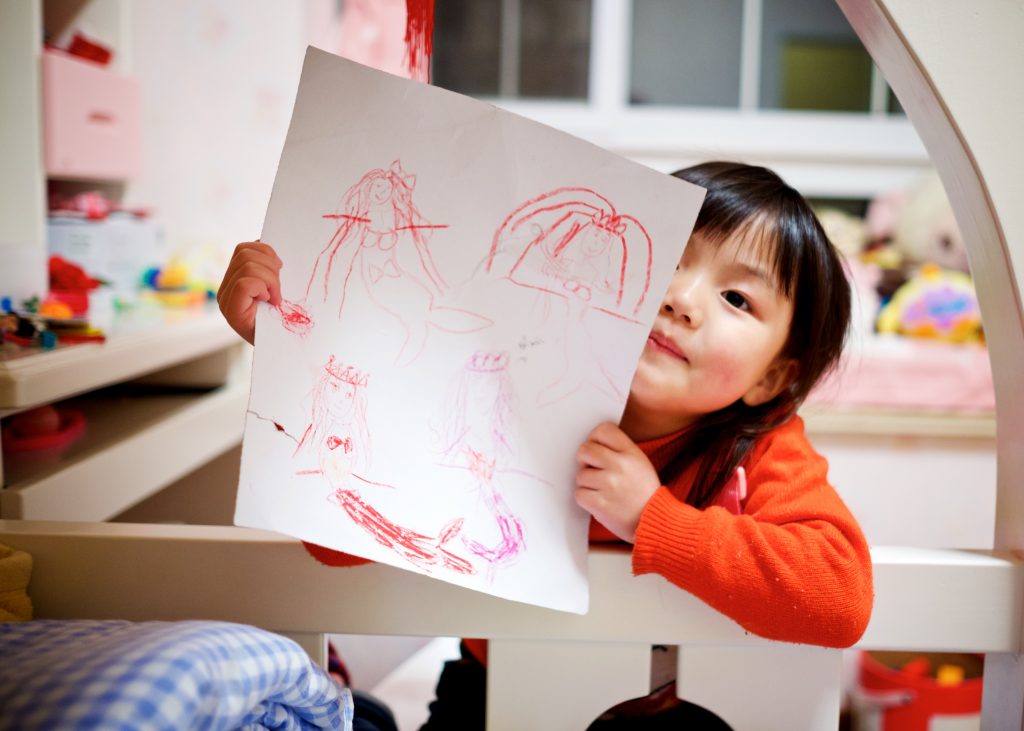 Criança menina mostrando um desenho para a câmera, representando as fases da criança.