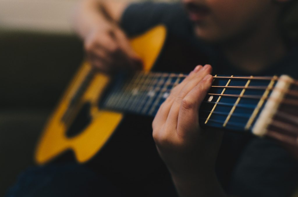 Criança tocando um violão para aprender inglês com música.