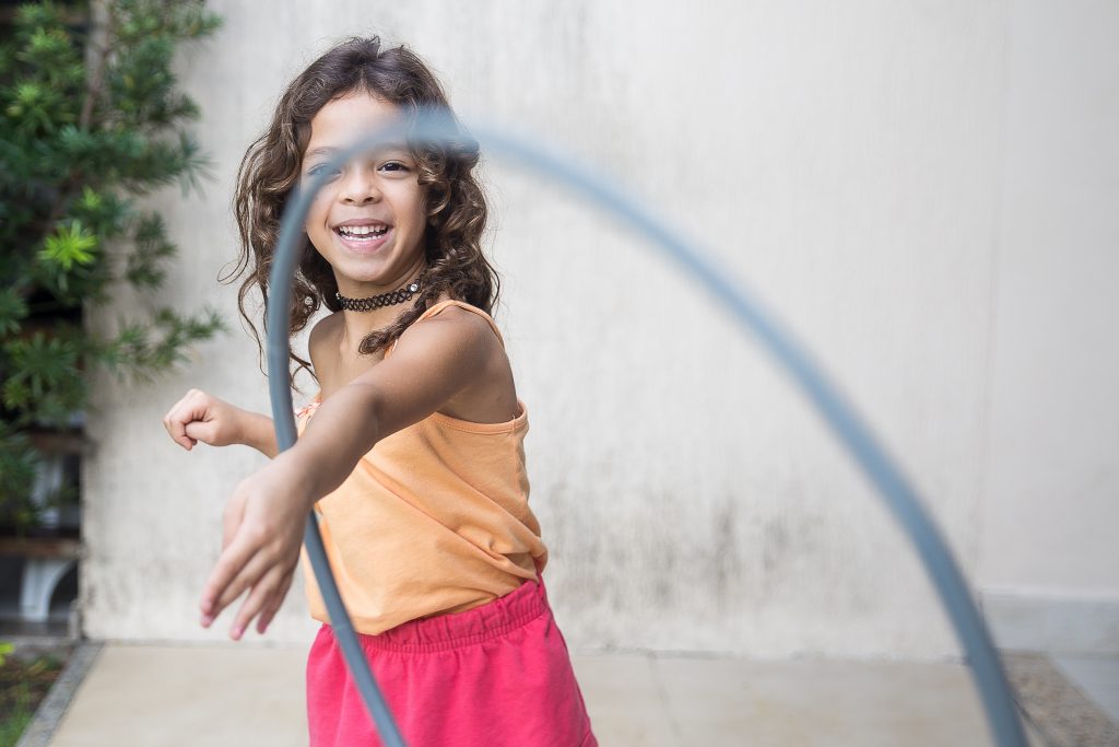 Criança menina desenvolvendo psicomotricidade infantil brincando com um bambolê.