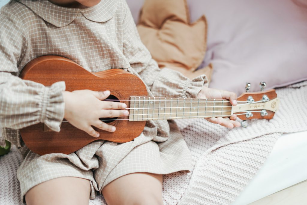 Criança tocando um ukulelê, representando a importância da música na educação infantil.
