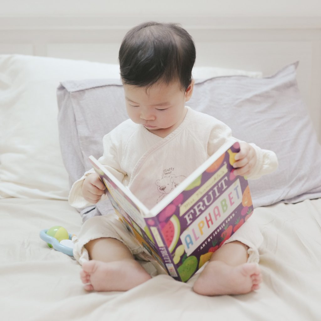 Criança lendo um livro infantil sentada em uma casa, exemplo de como incentivar a leitura em casa.