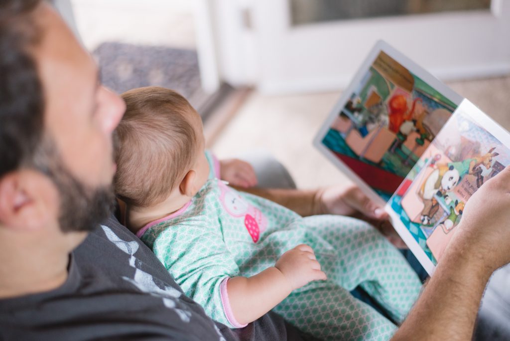 Bebê no colo do pai lendo um livro, mostrando como incentivar a leitura desde cedo.