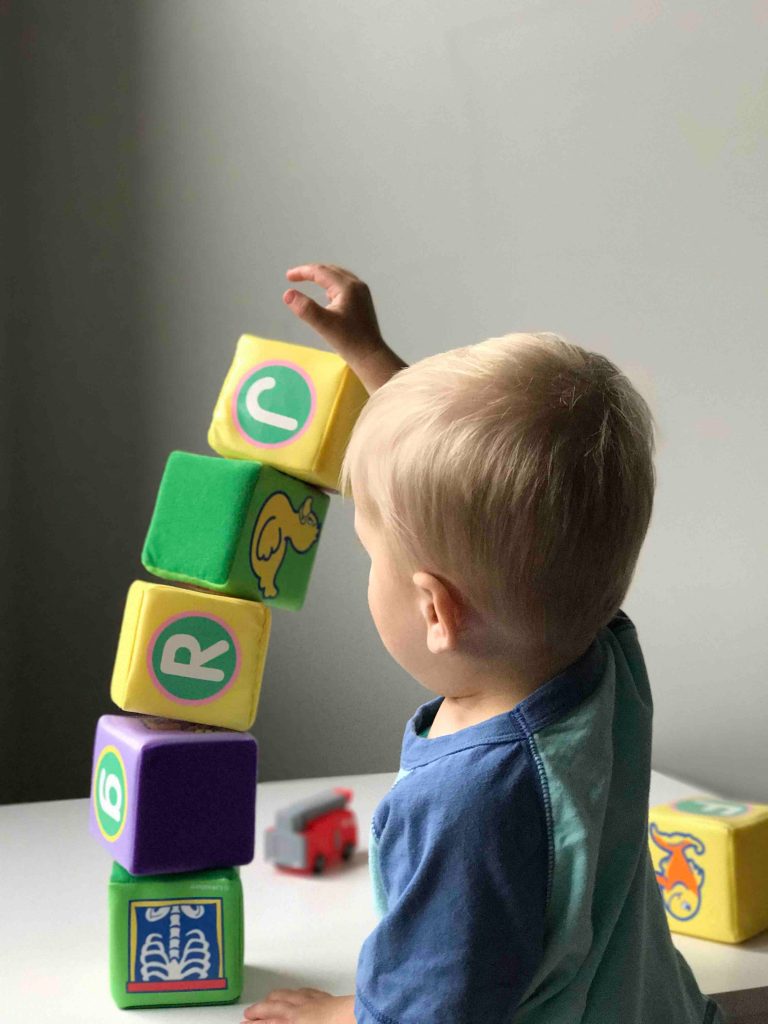 Menino exemplificando o desenvolvimento da criança ao brincar com blocos de pelúcia.