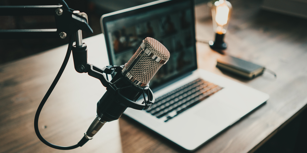Podcast para aprender inglês: imagem com laptop e microfone, sobre uma mesa.