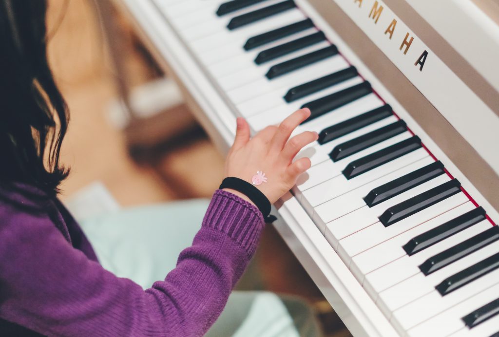 Visão aérea de uma criança tocando um teclado elétrico para aprender inglês com música.