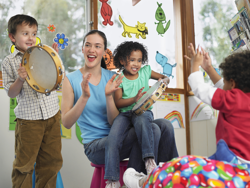 Jovem professora ensinando inglês para crianças de forma lúdica, por meio de instrumentos musicais e arte.