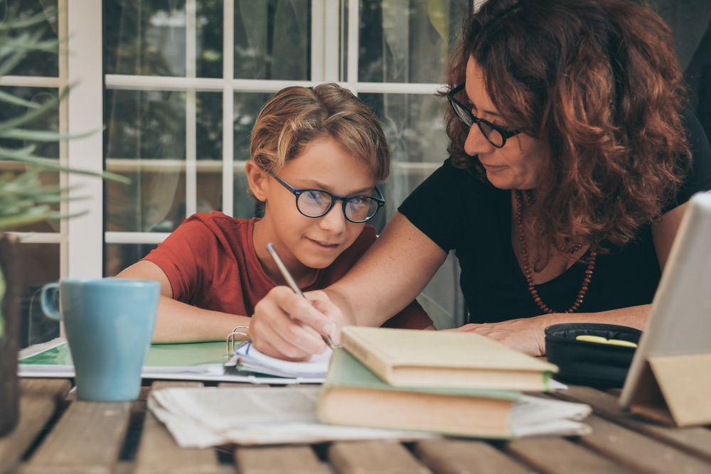 Mãe utilizando de técnicas para ajudar filho a desenvolver a concentração infantil. Os dois estão sentados, lado a lado,  executando atividades em livros.