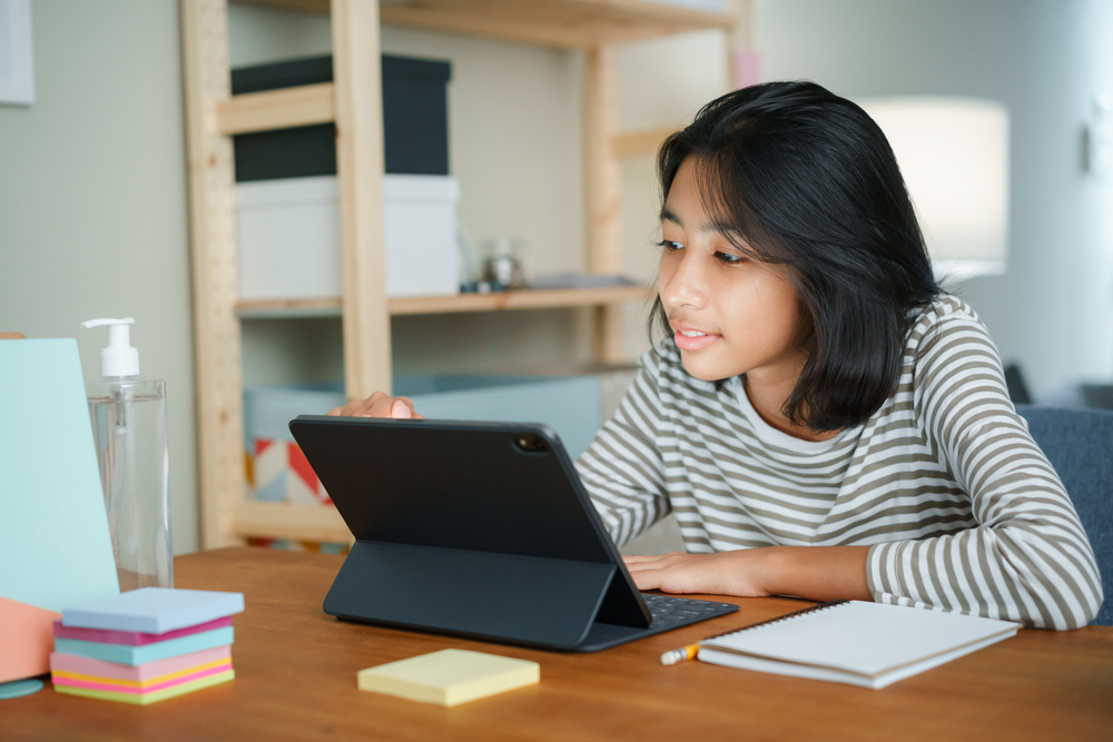 Garota com tablet na mesa do quarto: um exemplo de como aprender inglês de forma natural.