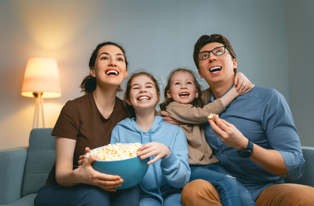 Família composta por: homem, mulher e duas filhas, reunida para assistir a dicas de filmes.