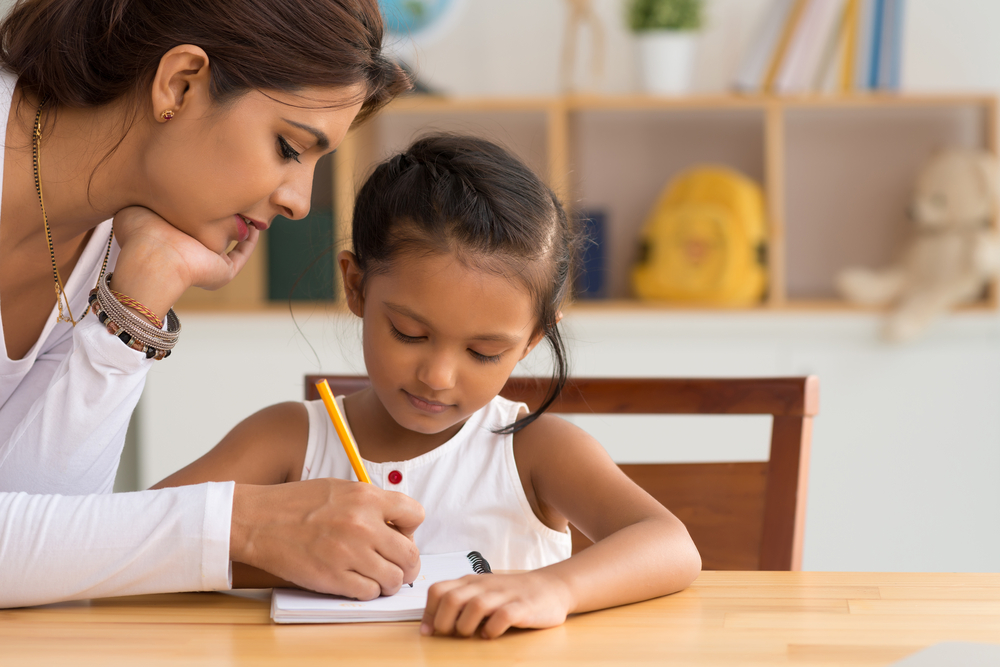 Ensino infantil: mãe ajudando sua filha a aprender a língua inglesa por meio dos deveres de casa.